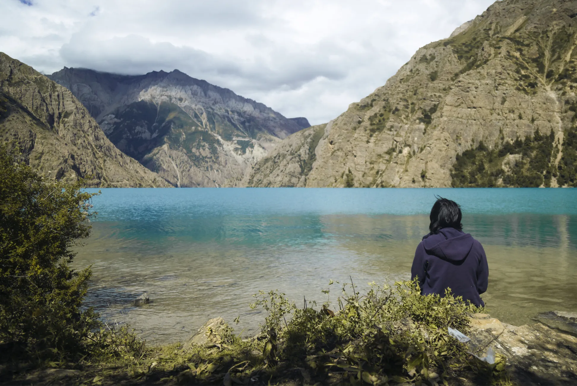 A trekker looks across the turquoise water of Phoksundo Lake towards the surrounding cliffs